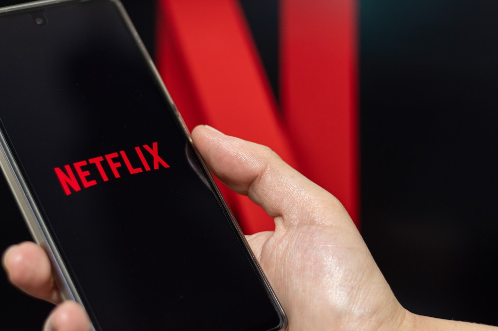 A person opening Netflix on their phone with the Netflix picture in the background.